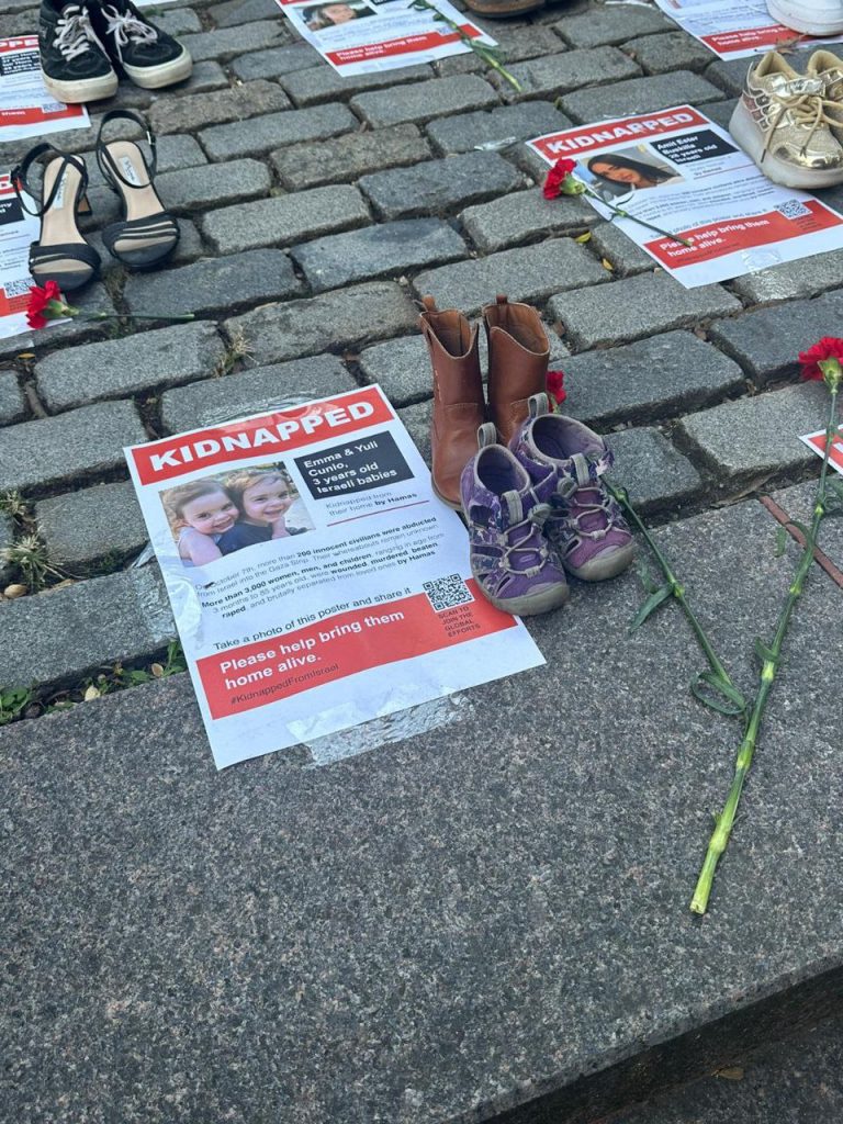 Пара детской обуви, цветы и листовка с текстом в память о жертвах ХАМАС